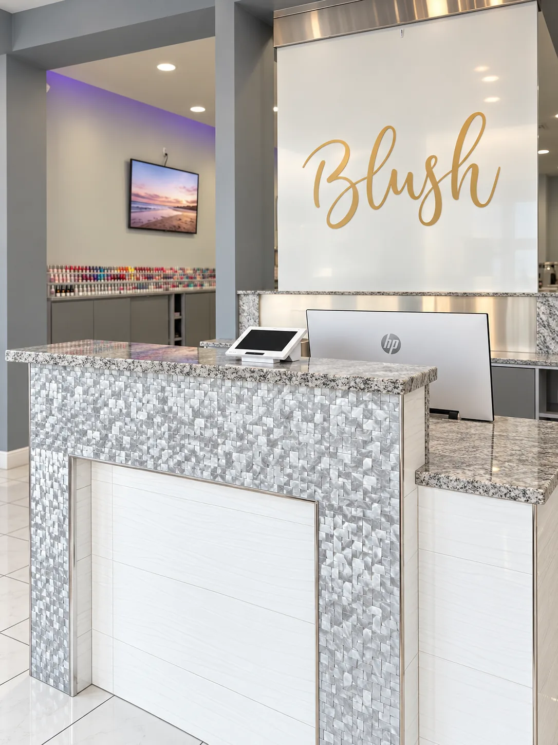 The Blush Nail Lounge front desk, with the gold Blush sign mounted on the white wall behind it