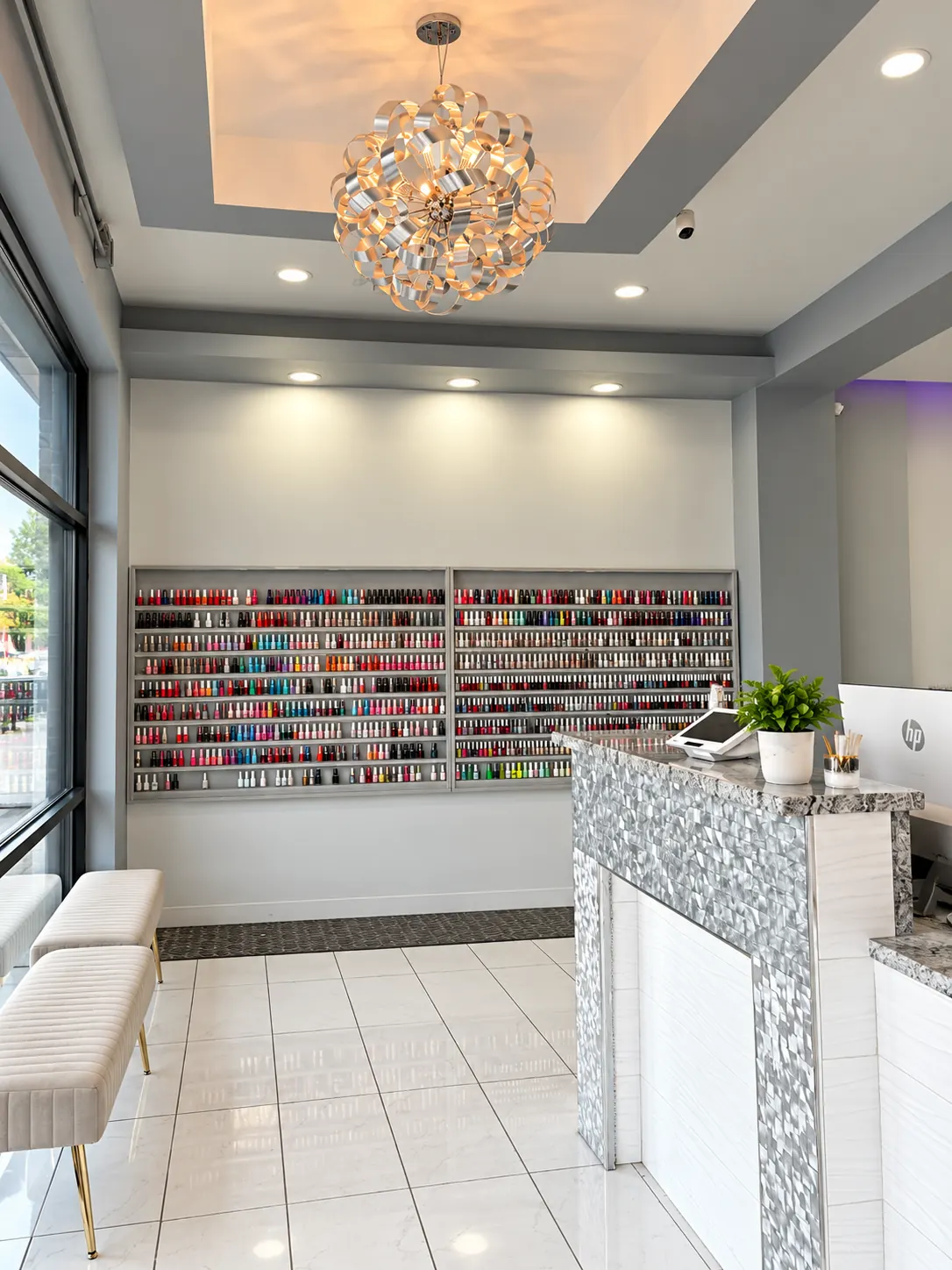 The reception desk and waiting area at Blush Nail Lounge, with a lit polish display and a sculptural chandelier